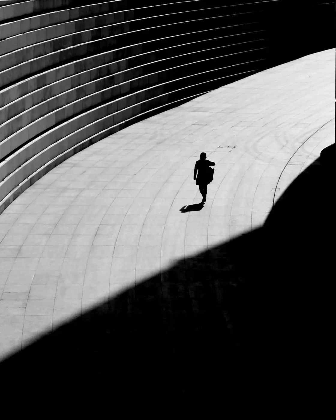 Lone runner crossing a curved concrete stadium wall